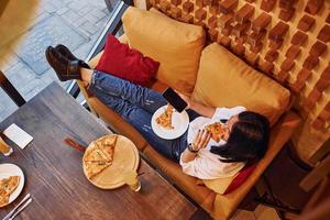 Young brunette sitting indoors with pizza and smartphone in hand photo