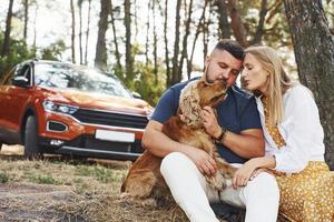 Couple with dog have weekend outdoors in the forest with car behind them photo