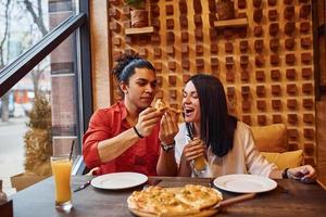 pareja joven multiétnica sentada en el interior juntos y comiendo pizza foto