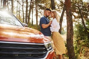 pareja abrazándose en el bosque cerca de un auto moderno foto