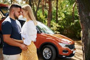 Couple embracing each other in the forest in front of modern car photo