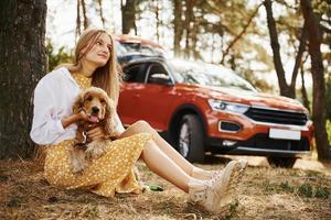 Leaning on the tree. Woman with her dog outdoors in the forest against automobile have good time photo