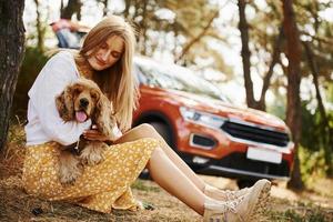 Leaning on the tree. Woman with her dog outdoors in the forest against automobile have good time photo