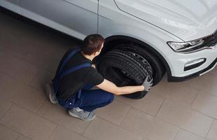 Top view of worker in black and blue uniform that is with car wheel working indoors photo