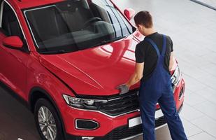 Top view of male worker in uniform that repairs red automobile photo