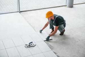 instalación de placas. hombre con uniforme gris y casco naranja trabaja en el interior de una gran oficina moderna durante el día foto