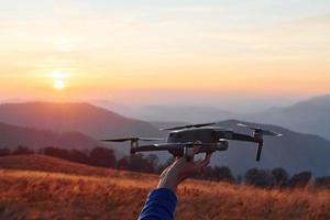 Man standing in the autumn field and holds drone in hand. Beautiful sunrise. Majestic landscape of mountains far away photo