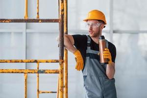 Man in grey uniform near construction takes break indoors in modern big office at daytime photo