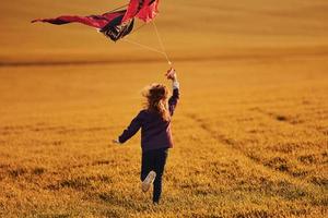 niña feliz corriendo con cometa en las manos en el hermoso campo foto