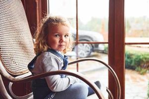 Portrait of cute little girl that sits in the chair indoors near the window photo