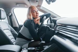 Side view of beautiful blonde in elegant clothes that sitting inside of modern car photo
