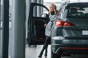 hermosa rubia con ropa elegante parada cerca de un auto nuevo y moderno foto