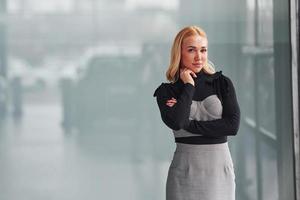 retrato de una hermosa rubia con ropa elegante que se encuentra en el interior contra un fondo gris foto