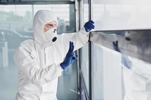 Male doctor scientist in lab coat, defensive eyewear and mask shows gesture through the window photo