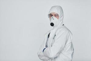 médico científico masculino en bata de laboratorio, anteojos defensivos y máscara de pie contra fondo blanco foto