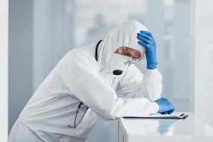 Tired doctor scientist in lab coat, defensive eyewear and mask takes break photo
