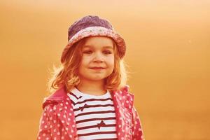 Portrait of cute little girl that standing outdoors illuminated by orange sunlight photo