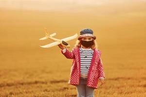 Illuminated by orange colored sunlight. Cute little girl have fun with toy plane on the beautiful field at daytime photo