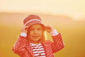 Portrait of cute little girl that standing outdoors illuminated by orange sunlight photo