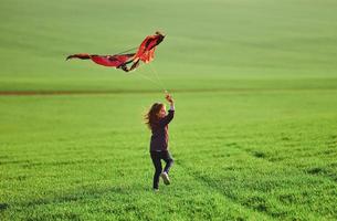 niña feliz corriendo con cometa en las manos en el hermoso campo foto