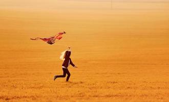 niña feliz corriendo con cometa en las manos en el hermoso campo foto
