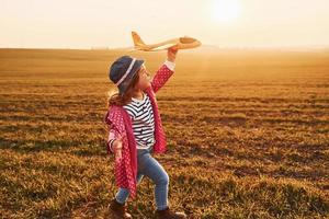 Cute little girl runs with toy plane on the beautiful field at sunny daytime photo