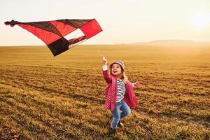 Happy little girl running with kite in hands on the beautiful field at sunrishe time photo