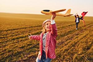 Two little girls friends have fun together with kite and toy plane on the field at sunny daytime photo