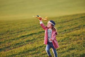 Cute little girl have fun with toy plane on the beautiful green field at sunny daytime photo