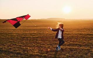 Happy little girl running with kite in hands on the beautiful field at sunrishe time photo