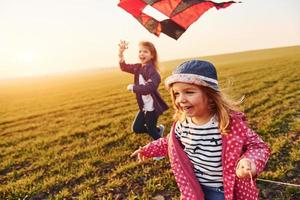 Two little girls friends have fun together with kite and toy car on the field at sunny daytime photo