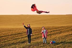 Two little girls friends have fun together with kite and toy car on the field at sunny daytime photo