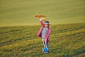 una niña linda se divierte con un avión de juguete en el hermoso campo verde durante el día soleado foto