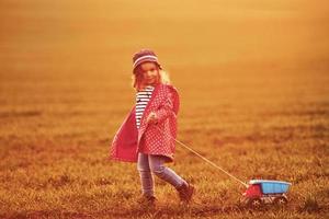 una linda niña camina con un camión de juguete en el hermoso campo durante el día soleado foto