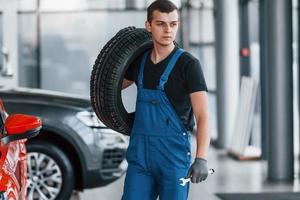 trabajador con uniforme negro y azul que sostiene la rueda del camión y tiene trabajo en el interior foto