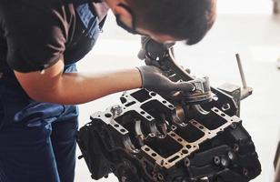 Professional repairman in black protective mask works with broken automobile engine photo