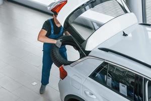 Worker in black and blue uniform places car wheel inside of white automobile photo