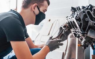 Professional repairman in black protective mask works with broken automobile engine photo