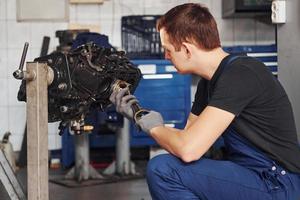 Professional repairman in garage works with broken automobile engine photo