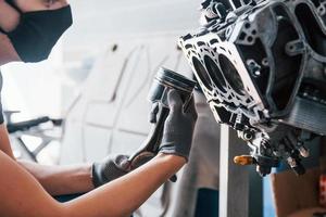 Professional repairman in black protective mask works with broken automobile engine photo