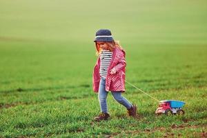 una linda niña camina con un camión de juguete en el hermoso campo durante el día soleado foto