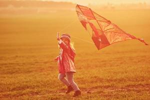Happy little girl running with kite in hands on the beautiful field at sunrishe time photo