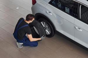 Top view of worker in black and blue uniform that is with car wheel working indoors photo