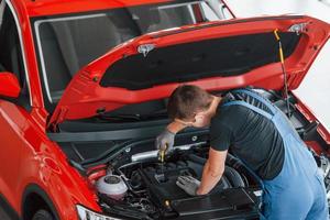 Top view of male worker in uniform that repairs red automobile photo