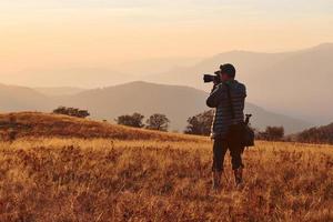 Male photographer standing and working at majestic landscape of autumn trees and mountains by the horizon photo