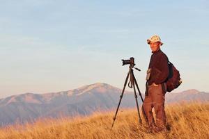 fotógrafo masculino de pie y trabajando en el majestuoso paisaje de árboles y montañas de otoño en el horizonte foto