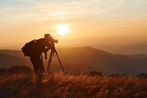 fotógrafo masculino de pie y trabajando en el majestuoso paisaje de árboles y montañas de otoño en el horizonte