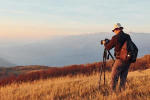 Male photographer standing and working at majestic landscape of autumn trees and mountains by the horizon photo