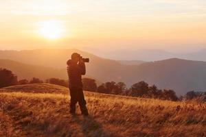 Male photographer standing and working at majestic landscape of autumn trees and mountains by the horizon photo