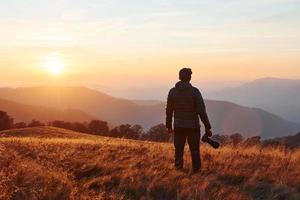 Male photographer standing and working at majestic landscape of autumn trees and mountains by the horizon photo